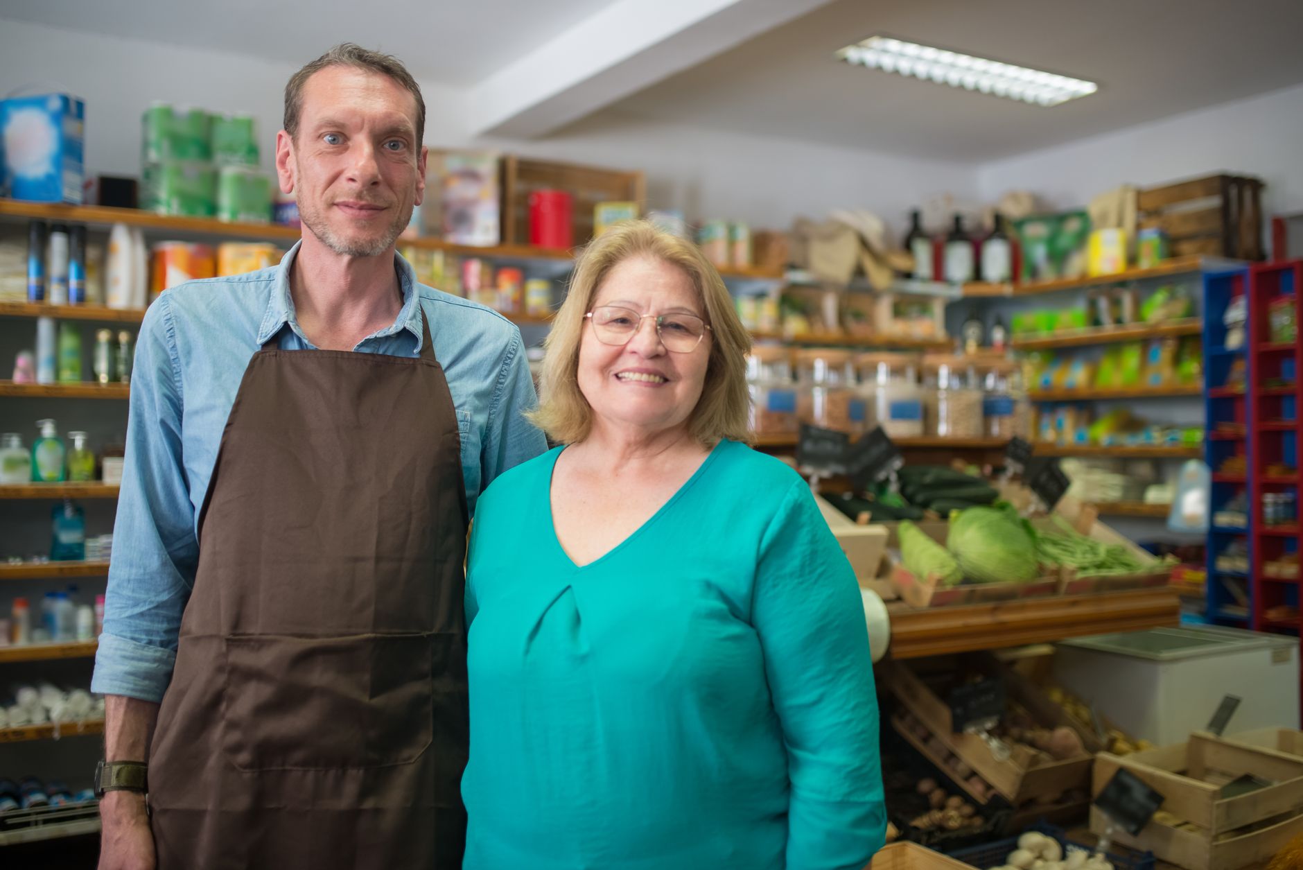 Deux commerçants souriants dans leur épicerie responsable, entourés de produits sur des étagères en bois
