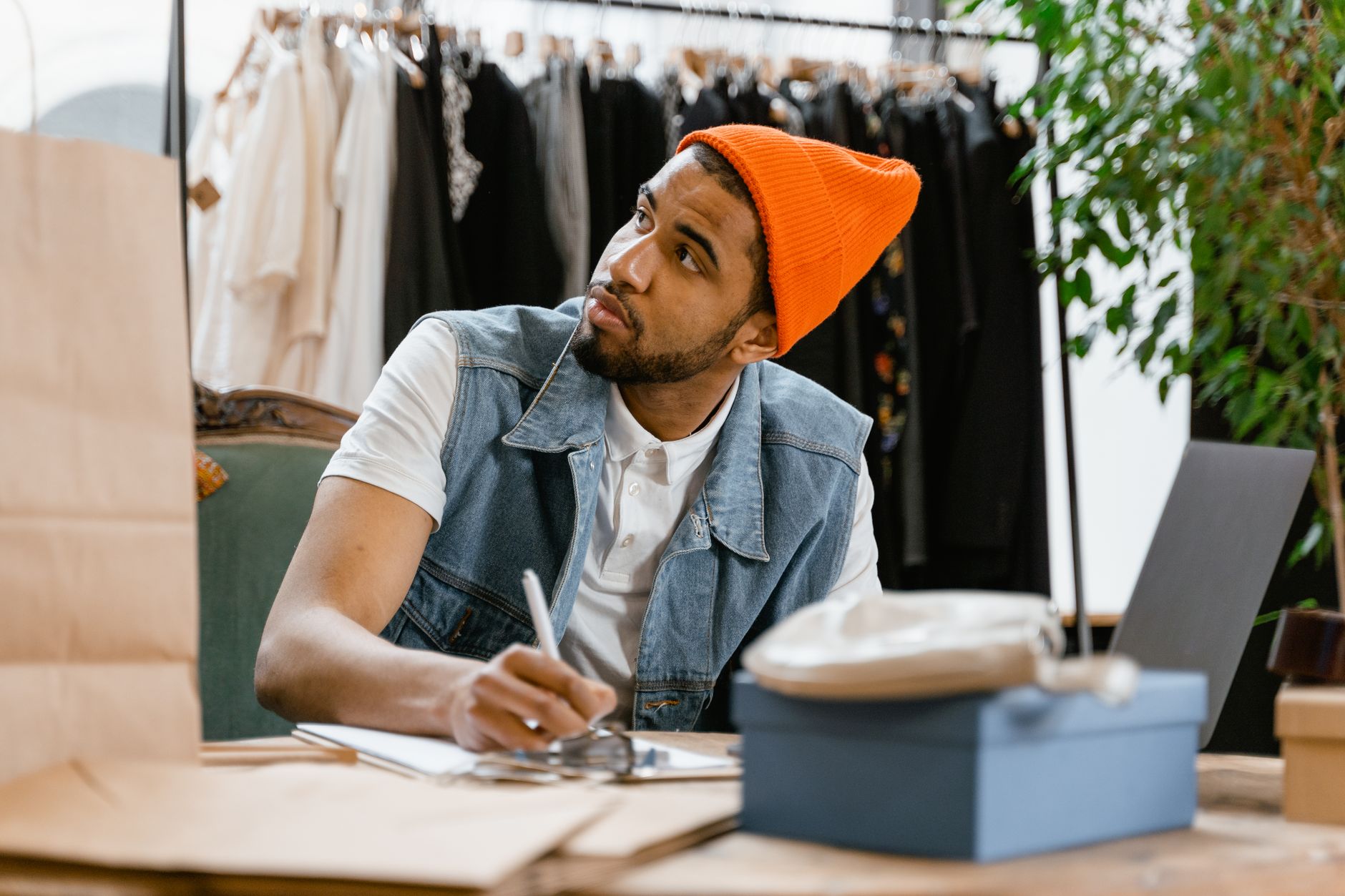 Un commerçant, dans sa boutique de vêtements, prend des notes à son comptoir avec un ordinateur portable