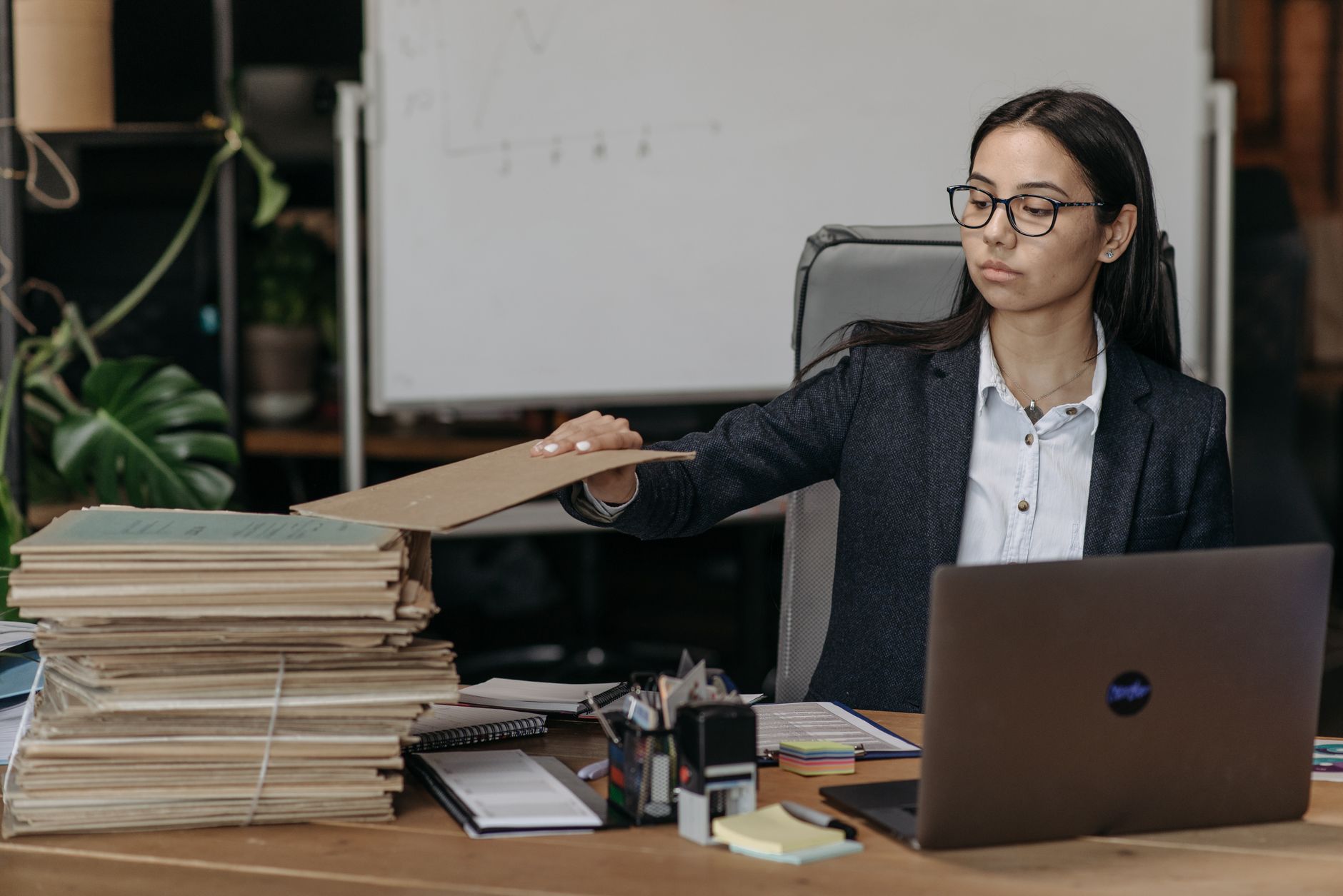 Une gestionnaire classe des dossiers de factures à son bureau, à côté de son ordinateur portable