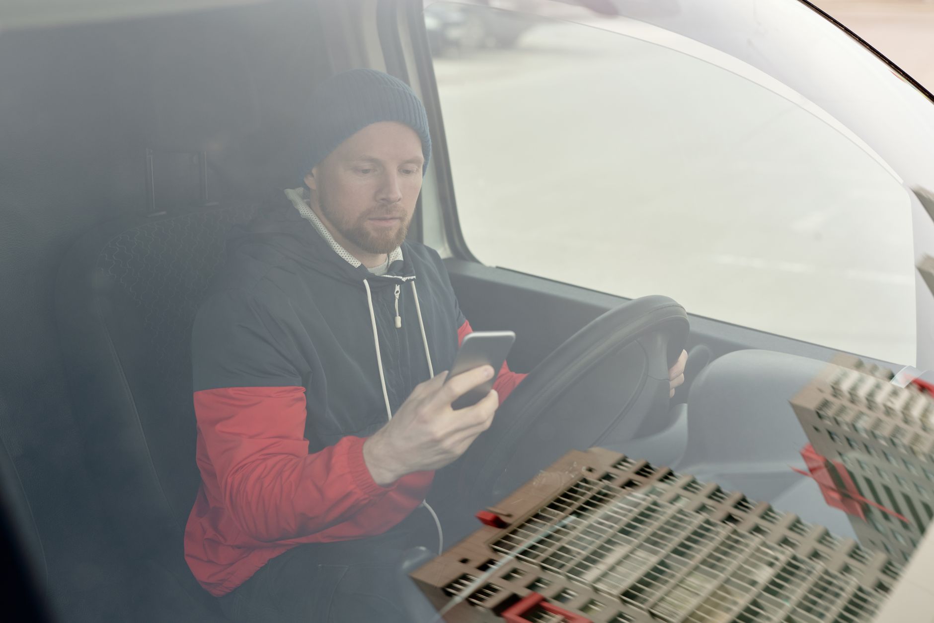 Un artisan installé au volant de sa camionnette consulte son téléphone avant de partir en intervention