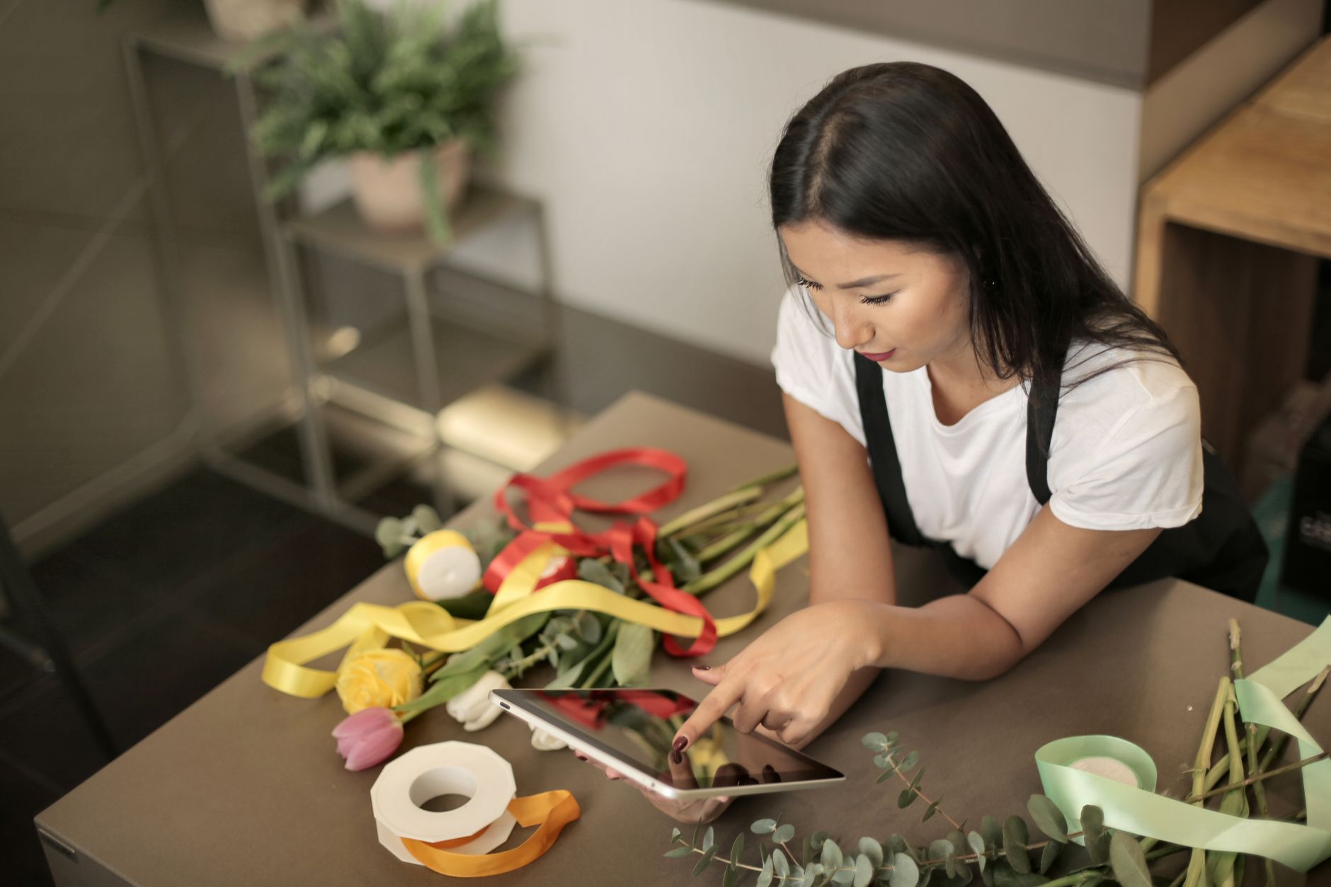 Une fleuriste consulte sa tablette dans son atelier, au milieu de ses fleurs et de ses rubans