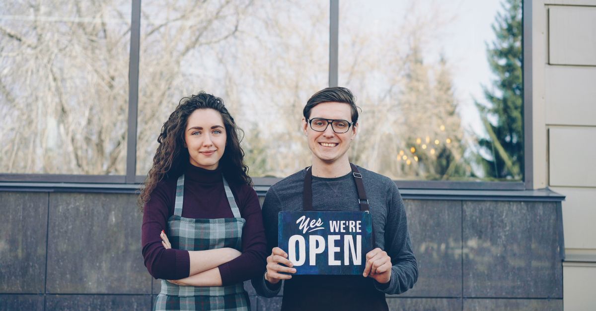 Deux jeunes commerçants en tablier, souriants devant leur boutique, prêts à ouvrir : l'esprit d'un projet d'expansion