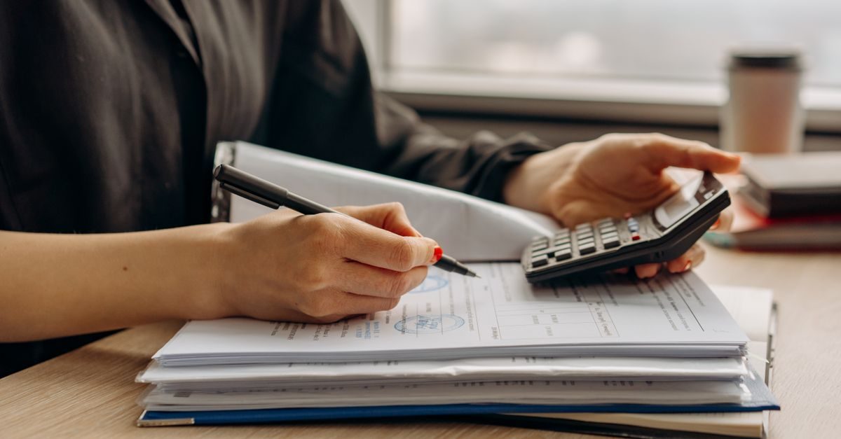 Un indépendant fait ses comptes : calculatrice à la main et pile de documents administratifs sur le bureau