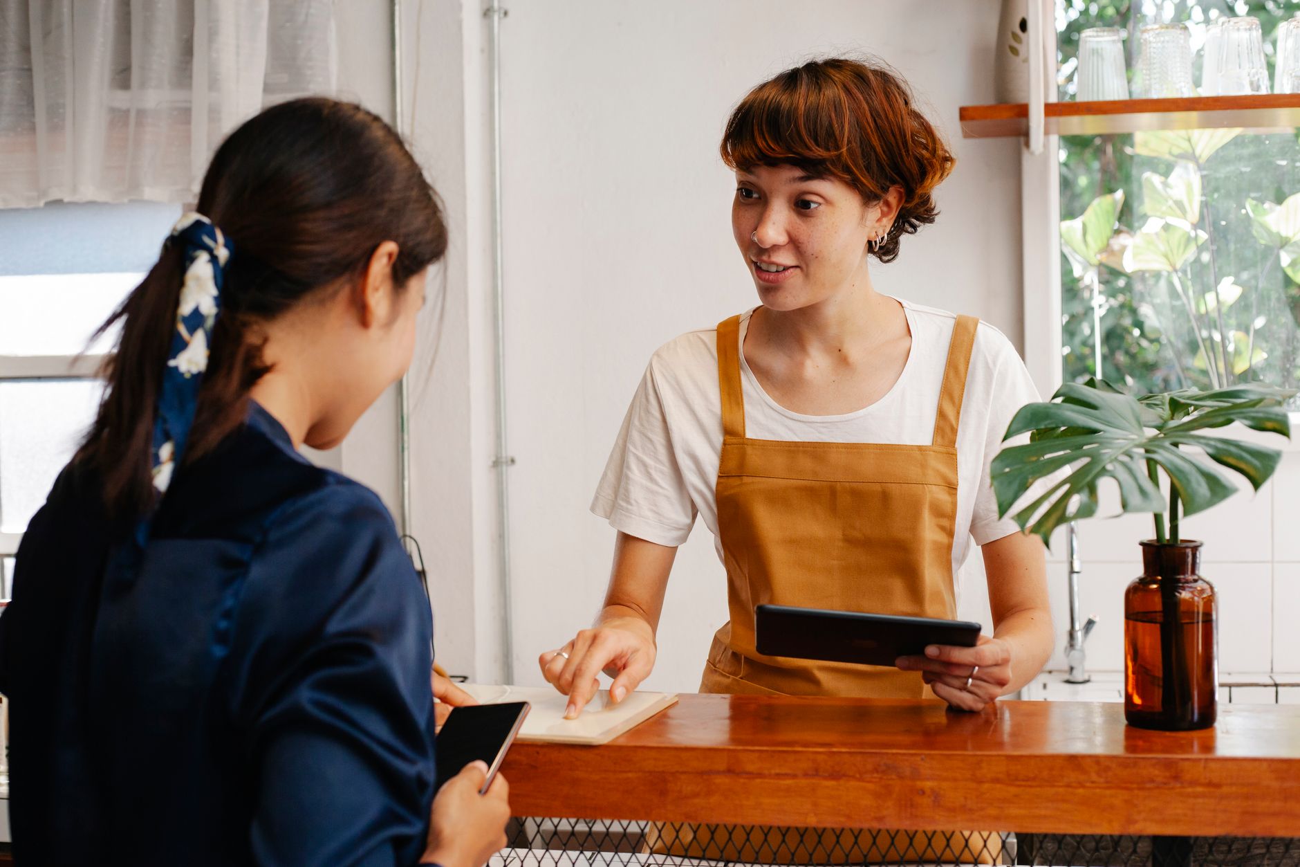 Une commerçante explique quelque chose à une cliente au comptoir de sa boutique, une tablette à la main