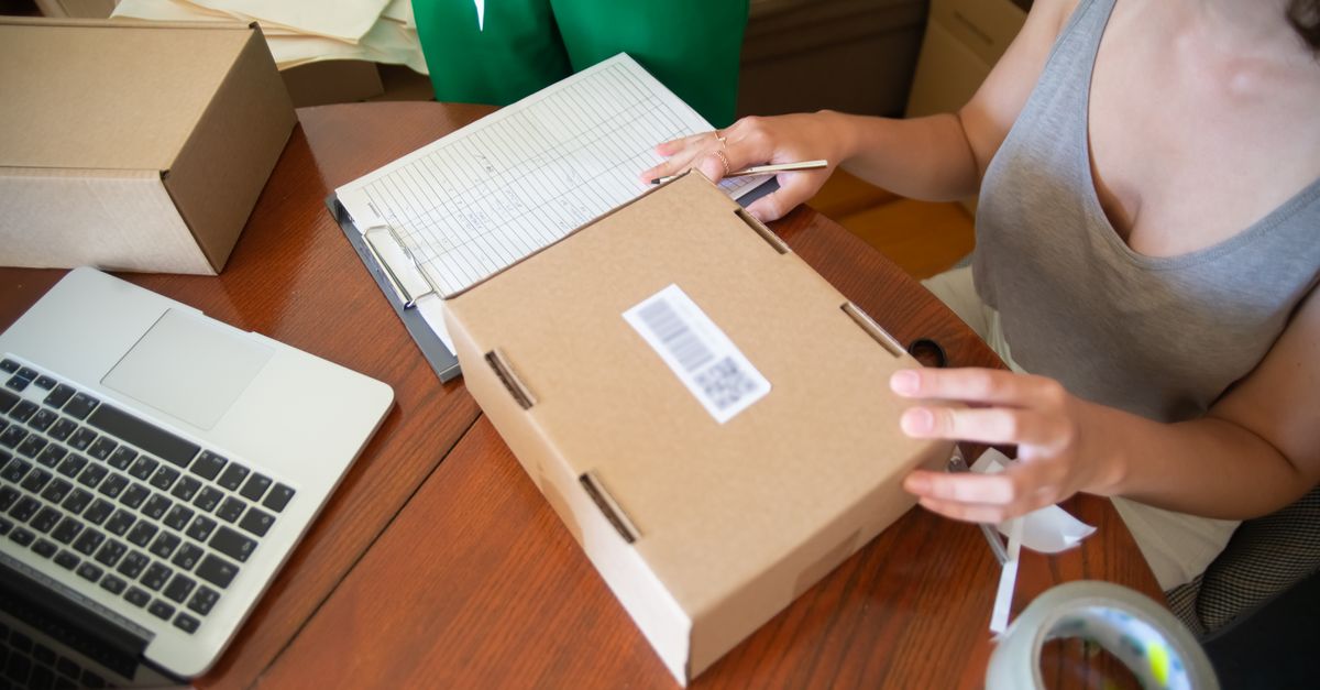 Une station d'expédition : un colis en carton portant une étiquette code-barres, un ordinateur portable et un bordereau