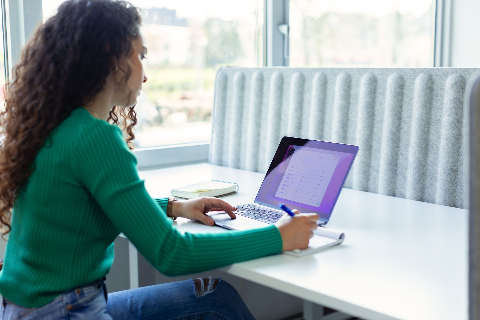 Une jeune indépendante organise son travail sur une application de type Notion sur son ordinateur portable, dans un espace de coworking lumineux
