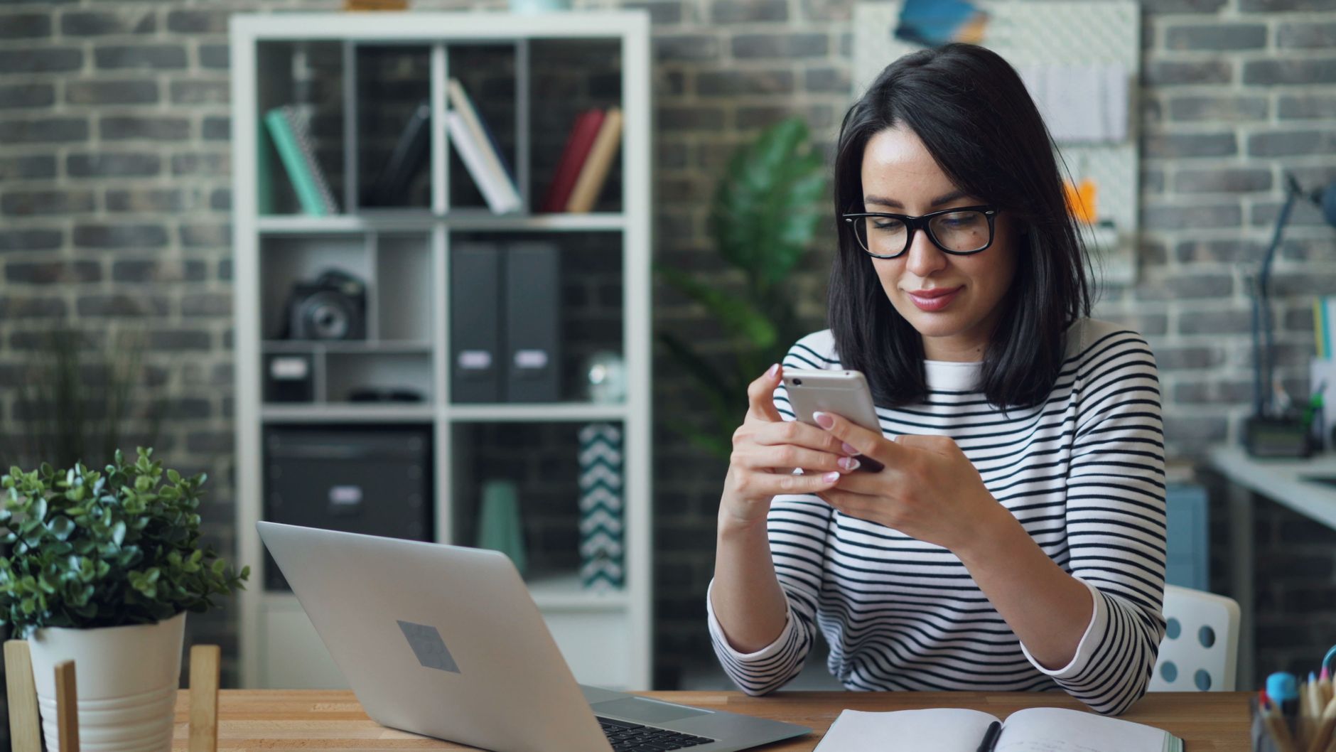 Une indépendante gère ses paiements et ses virements sur une application bancaire, entre son smartphone et son ordinateur portable, dans un bureau lumineux