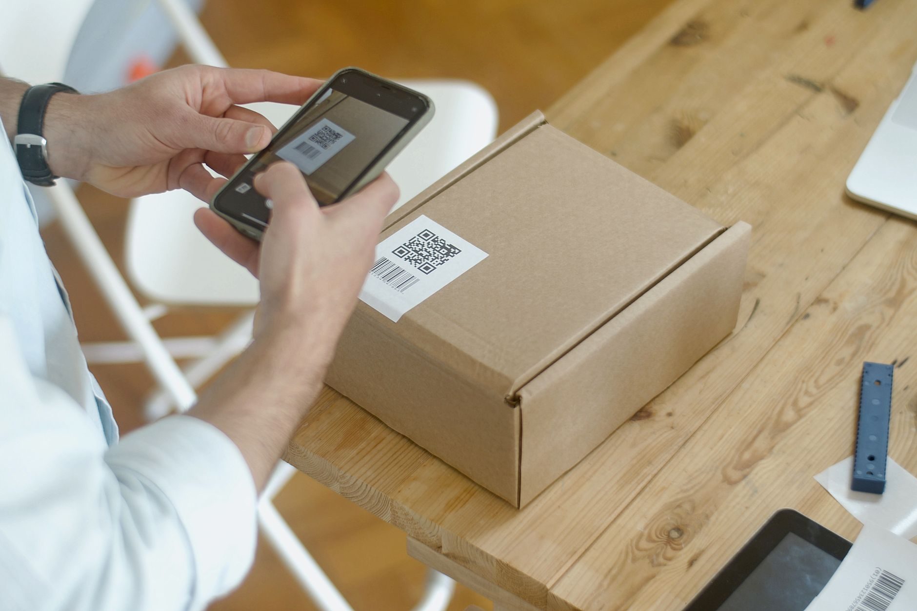 Professionnel en bureau européen qui scanne un QR code sur un colis avec son smartphone — contexte commerce ou logistique TPE