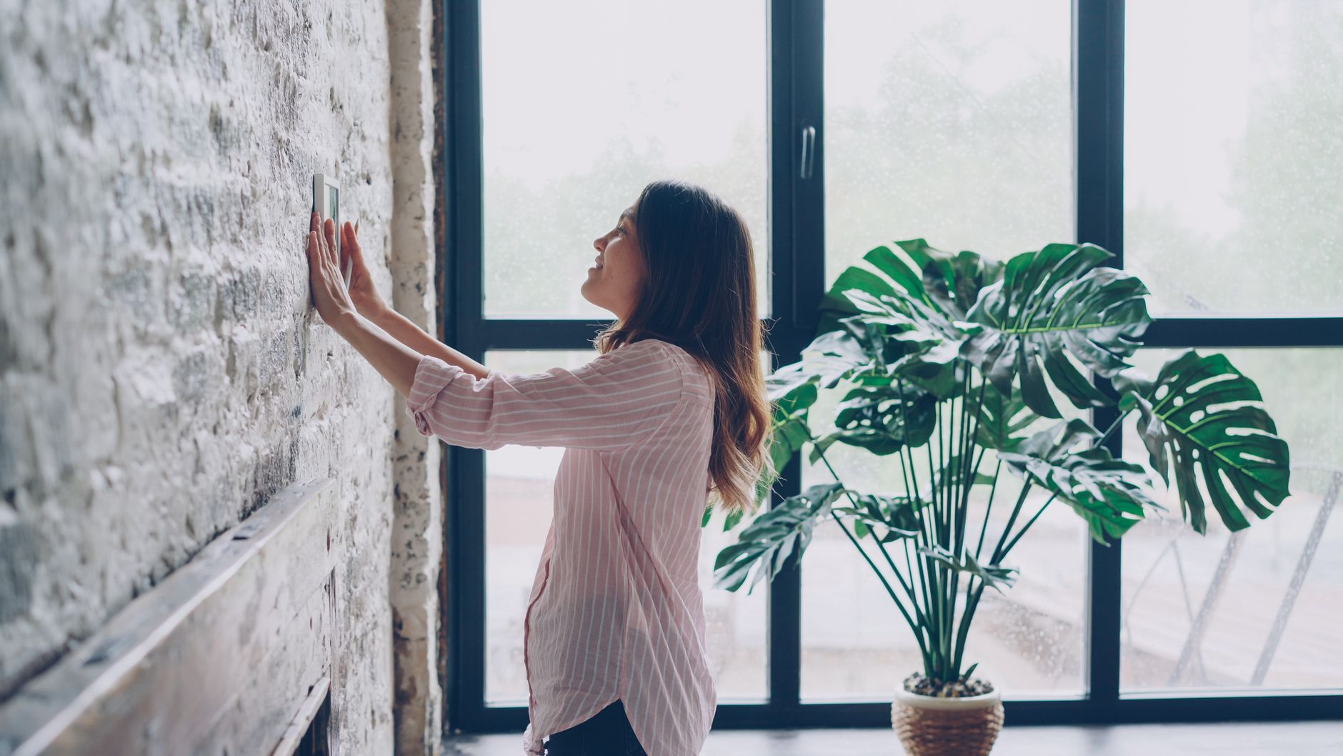 Une commerçante règle le thermostat mural de sa boutique dans une pièce lumineuse, geste de sobriété énergétique